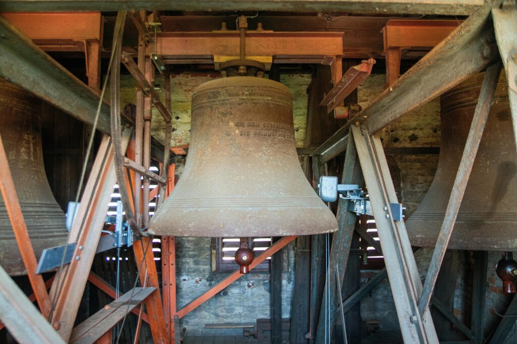 Rustic church bell tower interior showcasing vintage bronze bells in Leipzig, Germany.