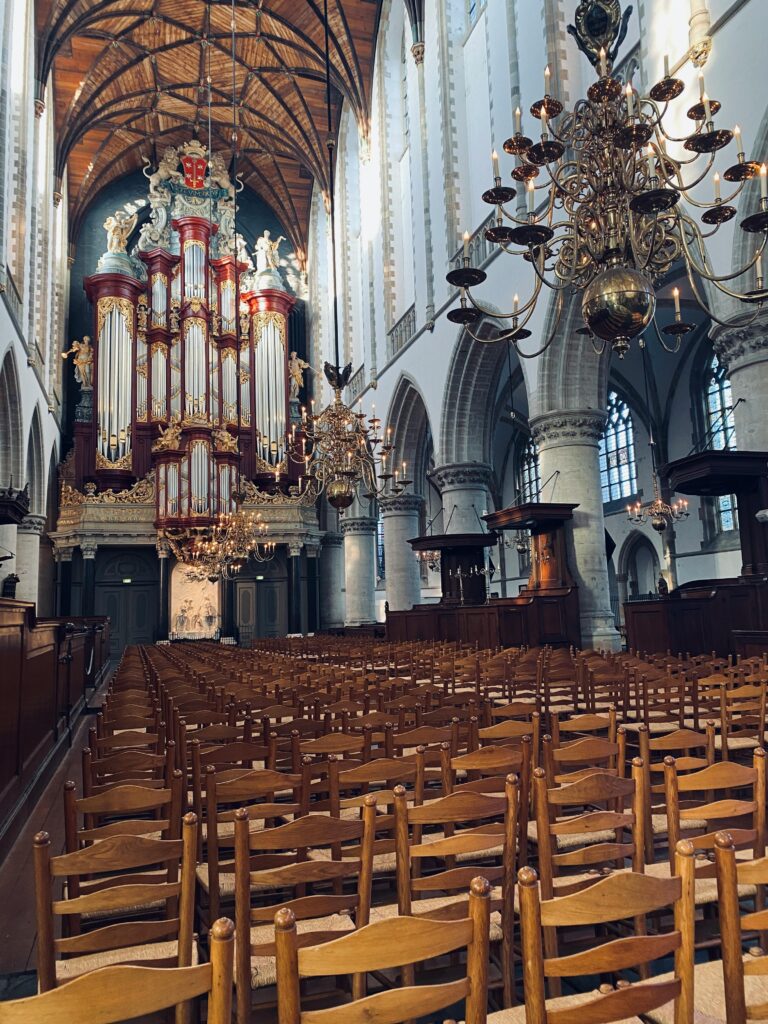A stunning pipe organ inside a historic Dutch cathedral with ornate chandeliers and wooden seating.
