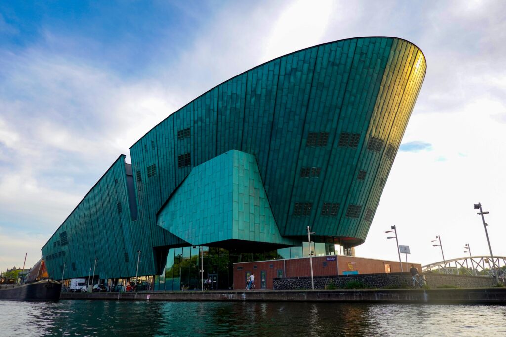 The NEMO Science Museum in Amsterdam with its iconic modern architecture beside a tranquil river.