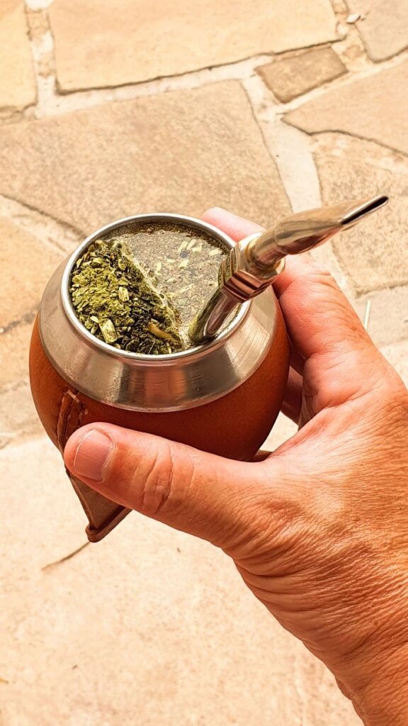 Hand holding a traditional yerba mate gourd with bombilla outdoors on a sunny day.